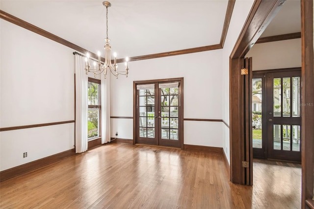 spare room with hardwood / wood-style flooring, ornamental molding, an inviting chandelier, and french doors