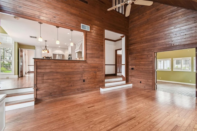 unfurnished living room featuring light wood-type flooring, a towering ceiling, wooden walls, and plenty of natural light