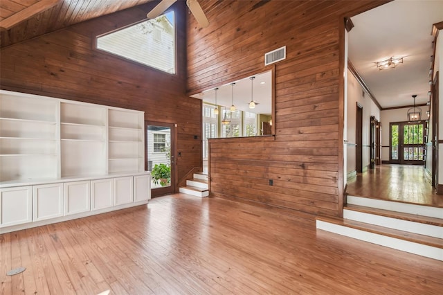 unfurnished living room with a towering ceiling, wood walls, ceiling fan, crown molding, and light hardwood / wood-style flooring