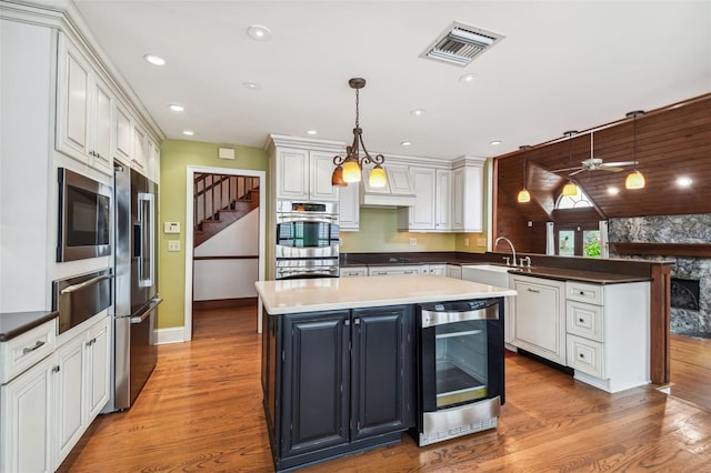 kitchen with appliances with stainless steel finishes, sink, wine cooler, hanging light fixtures, and hardwood / wood-style flooring