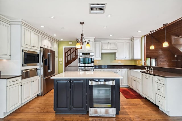 kitchen featuring sink, hanging light fixtures, stainless steel appliances, a center island, and beverage cooler