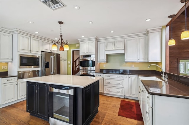 kitchen featuring wine cooler, sink, decorative light fixtures, a center island, and appliances with stainless steel finishes