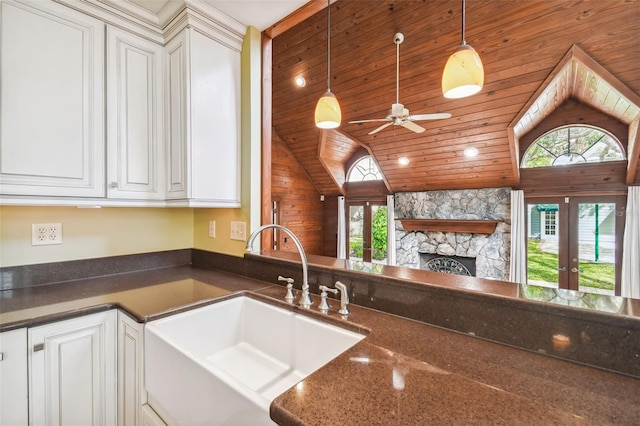 kitchen with pendant lighting, sink, white cabinetry, dark stone countertops, and a stone fireplace