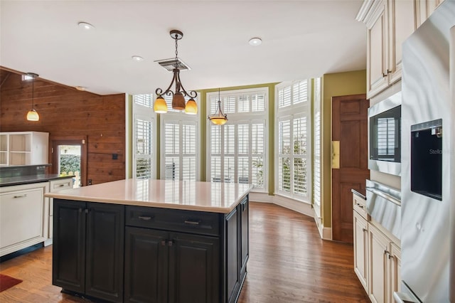 kitchen with appliances with stainless steel finishes, a kitchen island, wooden walls, decorative light fixtures, and dark wood-type flooring