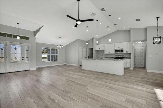 kitchen featuring appliances with stainless steel finishes, open floor plan, white cabinetry, a sink, and ceiling fan with notable chandelier