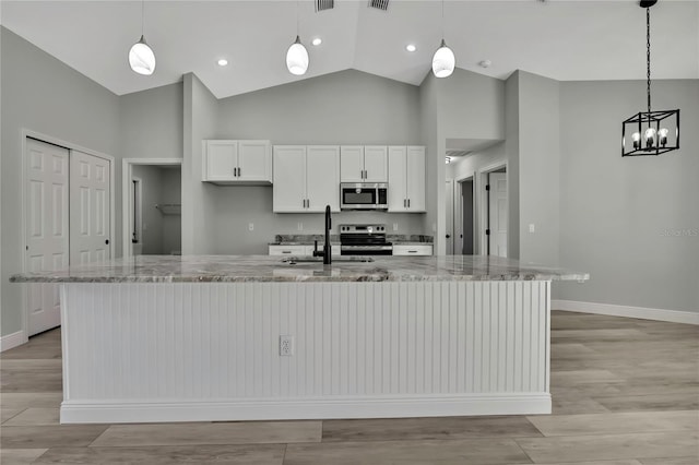 kitchen with a sink, white cabinets, appliances with stainless steel finishes, light stone countertops, and a large island with sink