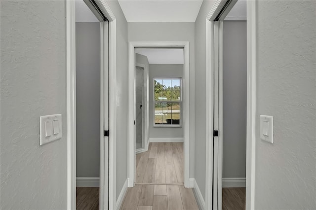 corridor with a textured wall, baseboards, and wood finished floors