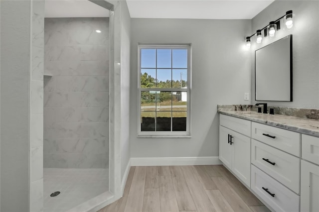 full bathroom with baseboards, a tile shower, wood finished floors, and vanity