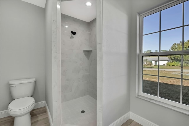 bathroom featuring toilet, baseboards, a tile shower, and wood finished floors