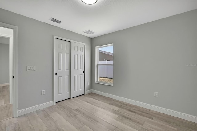 unfurnished bedroom featuring light wood-style floors, a closet, visible vents, and baseboards