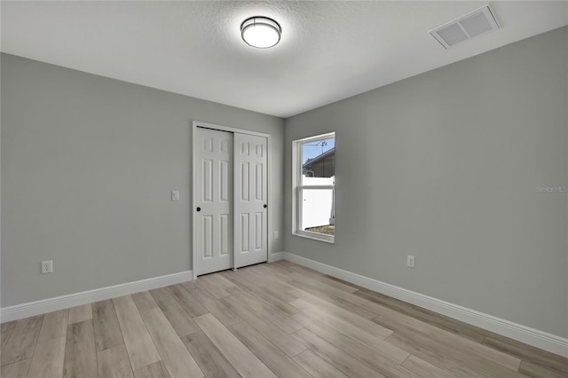 unfurnished room with visible vents, light wood finished floors, baseboards, and a textured ceiling