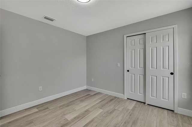 unfurnished bedroom with light wood-type flooring, baseboards, visible vents, and a closet