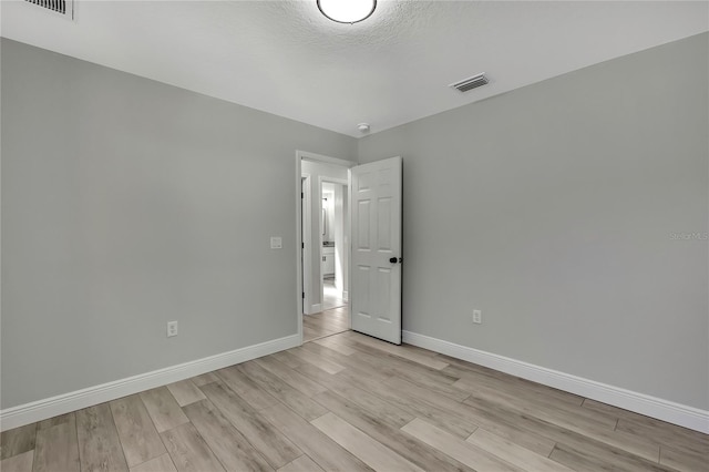 spare room with a textured ceiling, light wood finished floors, visible vents, and baseboards