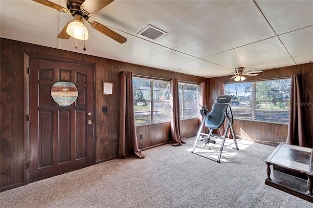 foyer entrance with a healthy amount of sunlight, light colored carpet, and wood walls