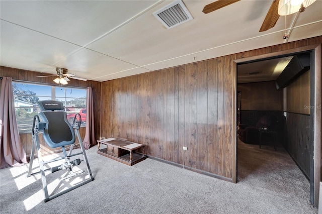 exercise area featuring ceiling fan, wooden walls, and carpet