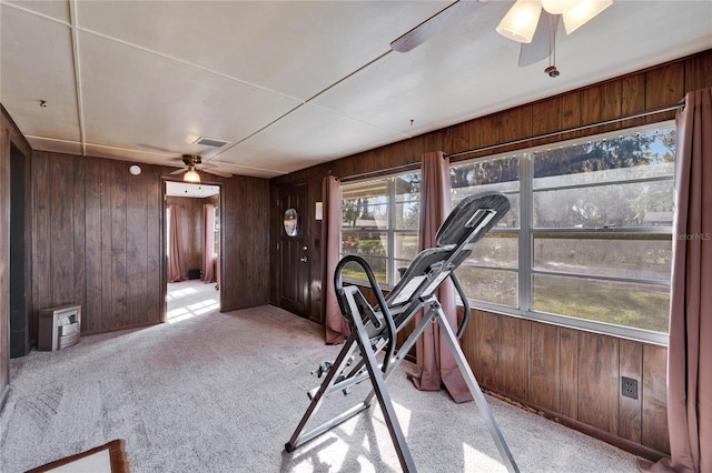 exercise room with ceiling fan, light carpet, and wood walls