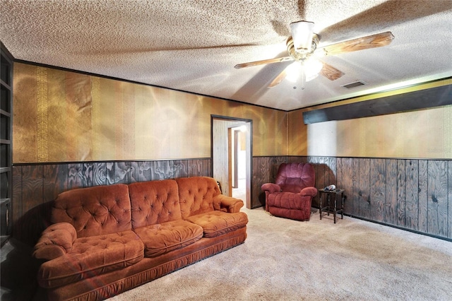 carpeted living room featuring ceiling fan, wooden walls, and a textured ceiling