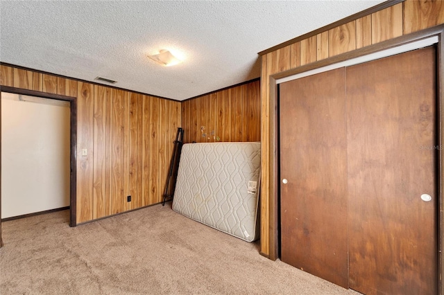 unfurnished bedroom featuring crown molding, wooden walls, a textured ceiling, light colored carpet, and a closet