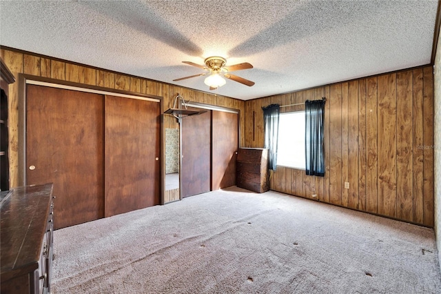 unfurnished bedroom with ceiling fan, wooden walls, a textured ceiling, two closets, and light colored carpet