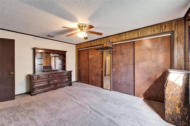 bedroom with ceiling fan, ornamental molding, a textured ceiling, light colored carpet, and wood walls