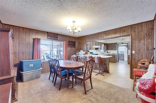 dining area with wooden walls, a wealth of natural light, light colored carpet, and a chandelier