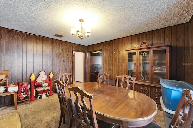 dining space with carpet, wooden walls, a notable chandelier, and a textured ceiling