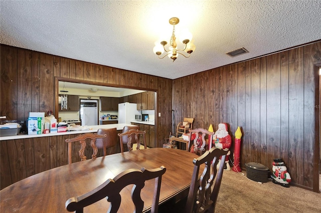 dining area featuring a textured ceiling, wood walls, a chandelier, and carpet