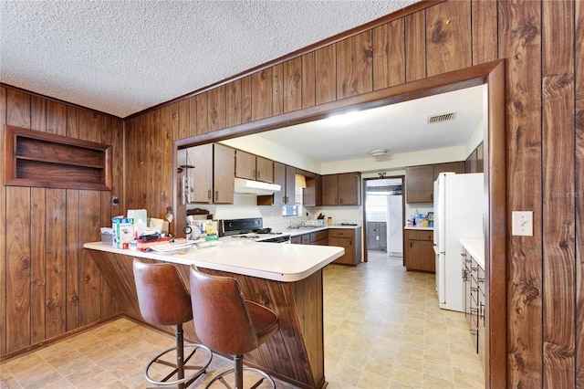 kitchen with white refrigerator, wooden walls, range, and kitchen peninsula