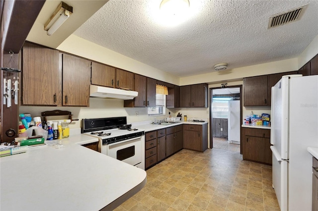 kitchen with dark brown cabinetry, sink, white appliances, and a textured ceiling