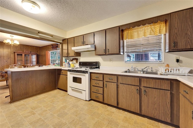 kitchen featuring sink, hanging light fixtures, wooden walls, white range oven, and kitchen peninsula