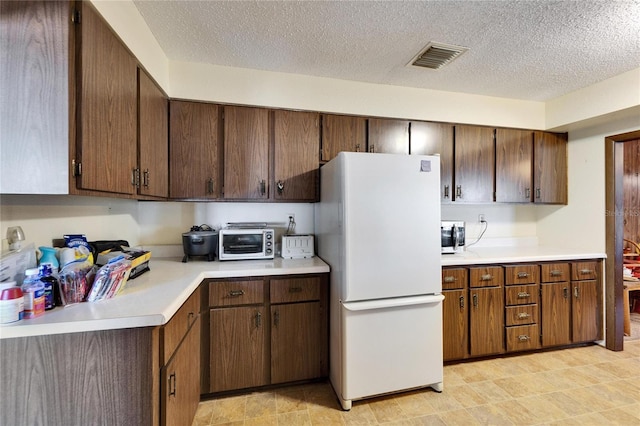 kitchen featuring dark brown cabinets, a textured ceiling, and white refrigerator