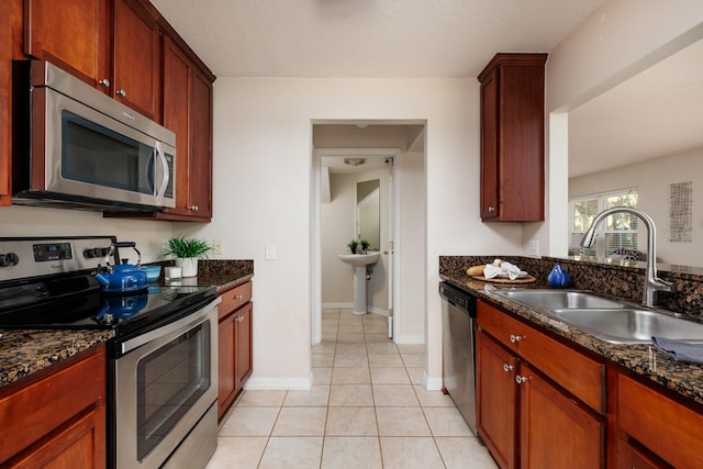 kitchen with stainless steel appliances, sink, dark stone countertops, and light tile patterned floors