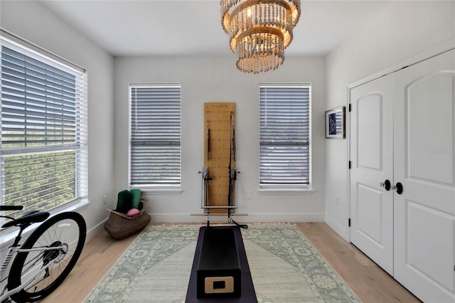 exercise room featuring a notable chandelier and light wood-type flooring