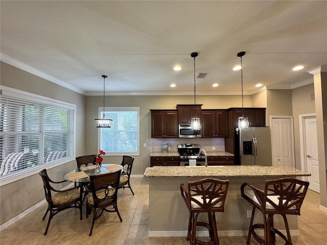 kitchen with dark brown cabinetry, a breakfast bar area, decorative light fixtures, an island with sink, and stainless steel appliances