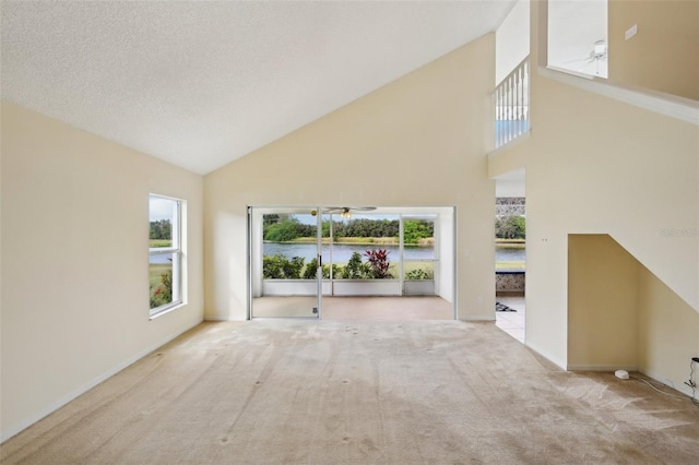 unfurnished living room with high vaulted ceiling, light colored carpet, a textured ceiling, and baseboards