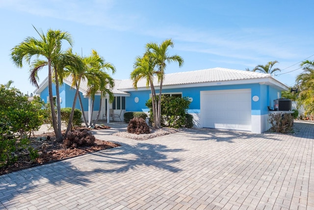 single story home with a garage, central AC, decorative driveway, and stucco siding