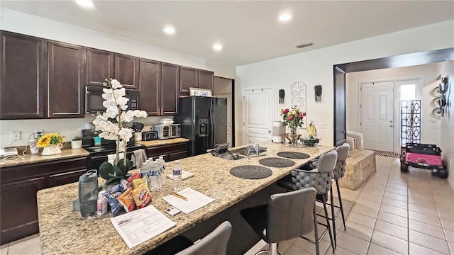 9362 Oglethorpe Dr, Groveland, FL 34736 - kitchen with black appliances, a breakfast bar area, light tile patterned floors, dark brown cabinetry, and light stone counters