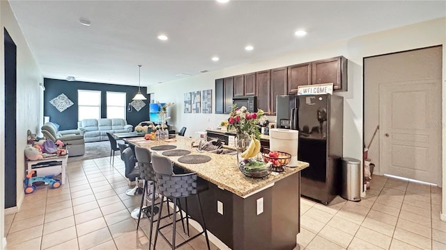 9362 Oglethorpe Dr, Groveland, FL 34736 - kitchen featuring black appliances, light tile patterned floors, dark brown cabinets, a kitchen island with sink, and a breakfast bar