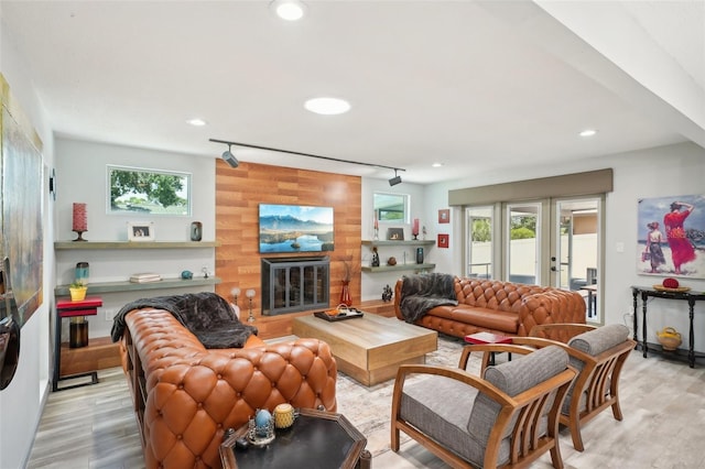 living room featuring a large fireplace, plenty of natural light, wooden walls, and light hardwood / wood-style flooring