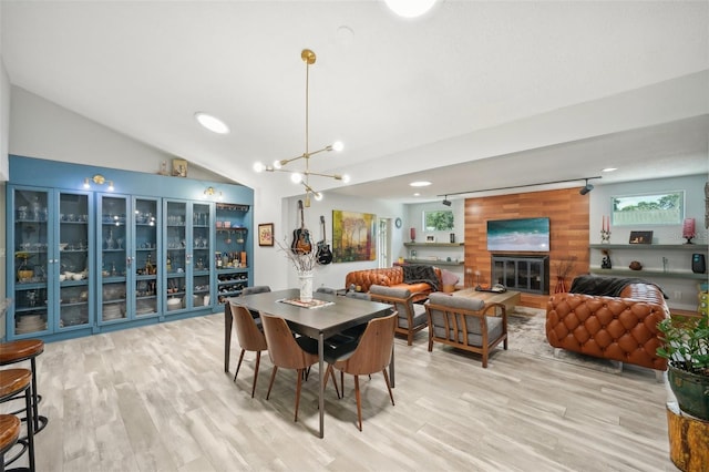 dining area with a notable chandelier, vaulted ceiling, wood walls, and light wood-type flooring