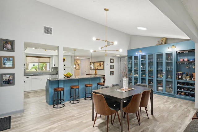 dining area with sink, a notable chandelier, light hardwood / wood-style floors, and high vaulted ceiling