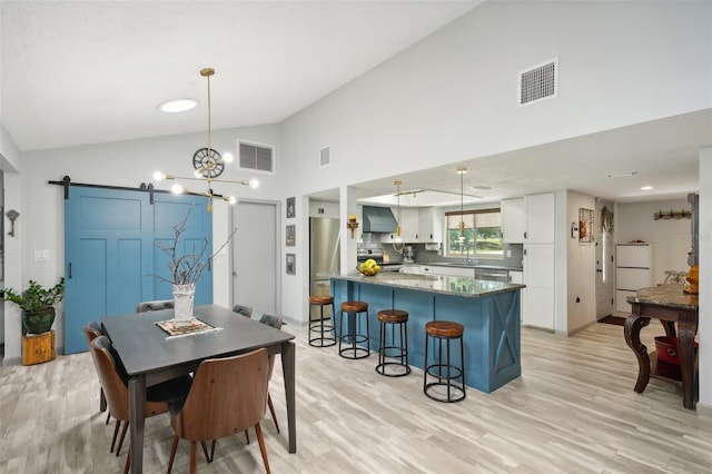 dining area featuring high vaulted ceiling, a barn door, sink, and light hardwood / wood-style flooring