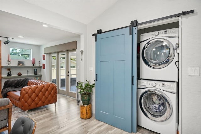 clothes washing area featuring french doors, stacked washer / drying machine, a barn door, and light hardwood / wood-style flooring