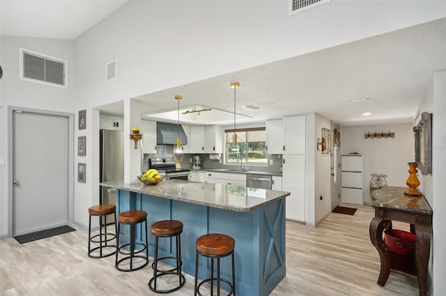 kitchen with pendant lighting, dark stone countertops, stainless steel appliances, white cabinets, and wall chimney exhaust hood