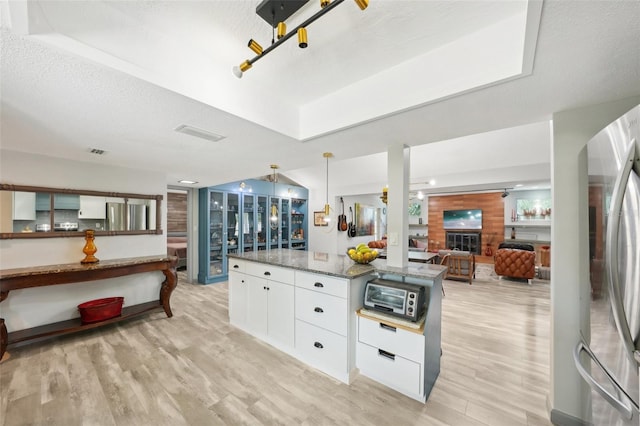 kitchen with pendant lighting, stainless steel refrigerator, white cabinetry, dark stone countertops, and light wood-type flooring