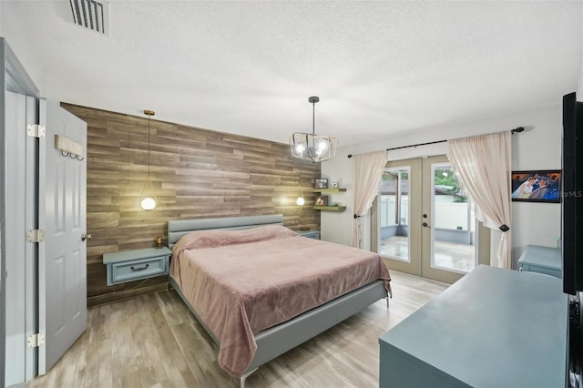 bedroom featuring french doors, wood walls, a textured ceiling, light wood-type flooring, and access to exterior