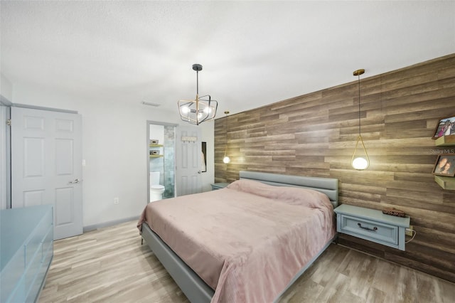 bedroom with light hardwood / wood-style flooring, a notable chandelier, wooden walls, and ensuite bathroom