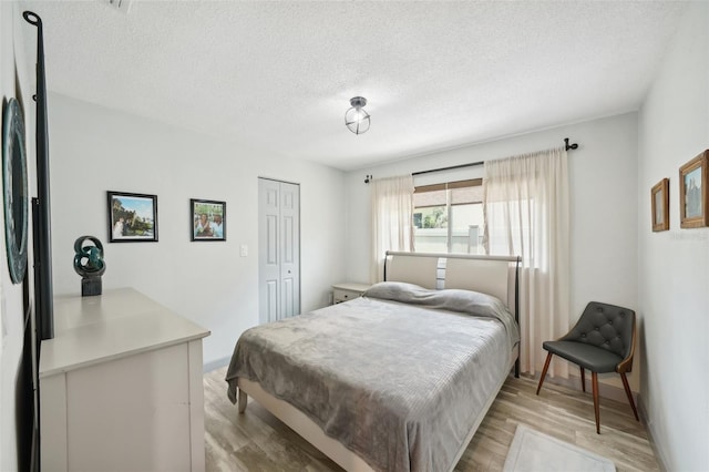 bedroom featuring black fridge, a closet, a textured ceiling, and light wood-type flooring