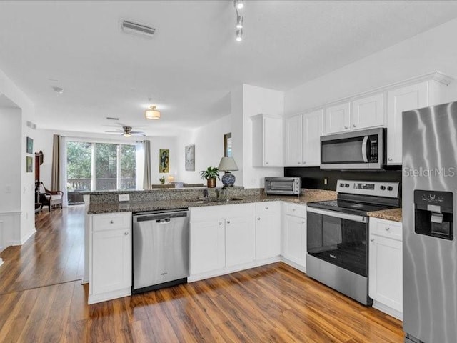 kitchen with white cabinetry, appliances with stainless steel finishes, kitchen peninsula, and dark stone counters