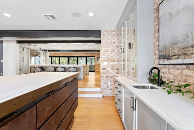 kitchen featuring dark brown cabinetry, sink, brick wall, light hardwood / wood-style floors, and white cabinets